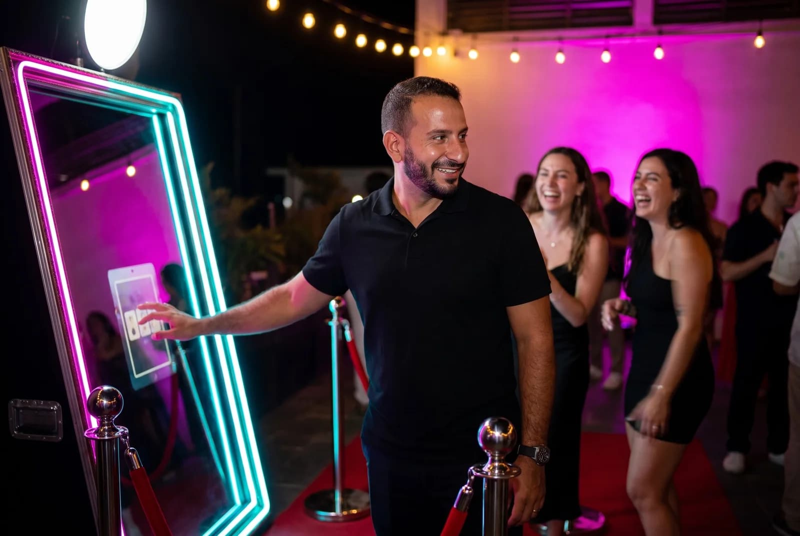 יוני טוביאנה מכוון את מסך המירור אייקס במהלך אירוע ערב, אורחים צוחקים ברקע